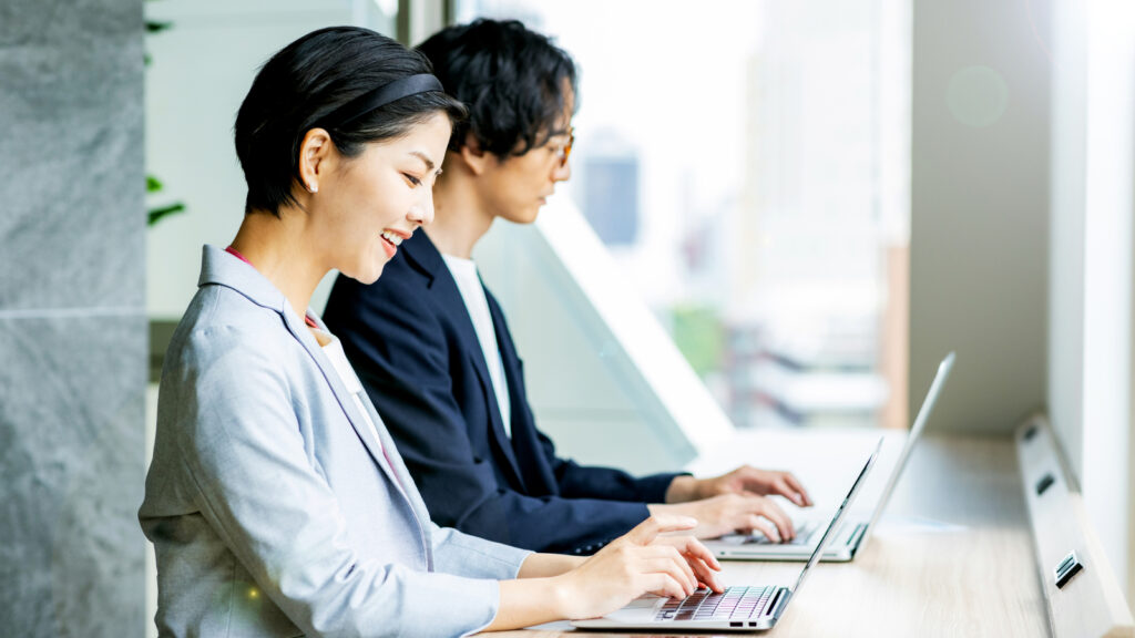 並んでノートパソコンで作業する社員
